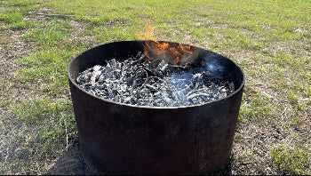 Biochar ring with burning wood and embers in a grassy area