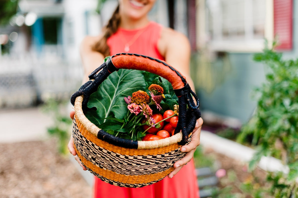 Person holding a woven basket with fresh produce in an outdoor setting